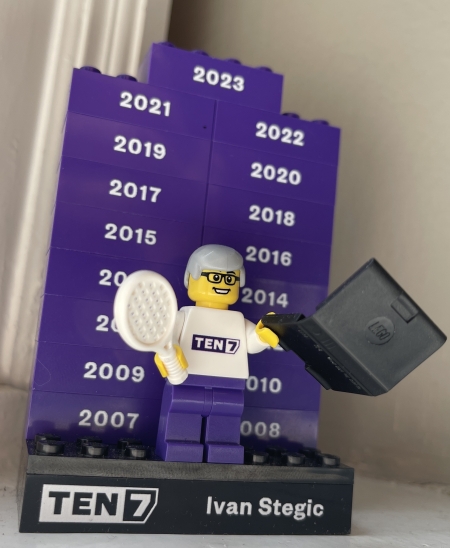 A Lego mini-figurine with grey hair and glasses, holding a tennis racket and a laptop, on a platform that says TEN7 and Ivan Stegic, plus stacks of bricks behind him for the years 2007 - 2023
