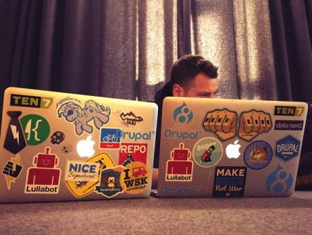 Two MacBook Airs on a table with lots of stickers and a head poking over the right one