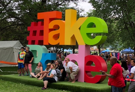 People standing in front of a giant TakePride sign in Loring Park