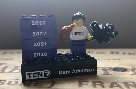 A Lego mini-figurine with black hair, holding a croissant and a cinema film camera, on a platform that says TEN7 and Dani Adelman plus four bricks for the years 2020 through 2023